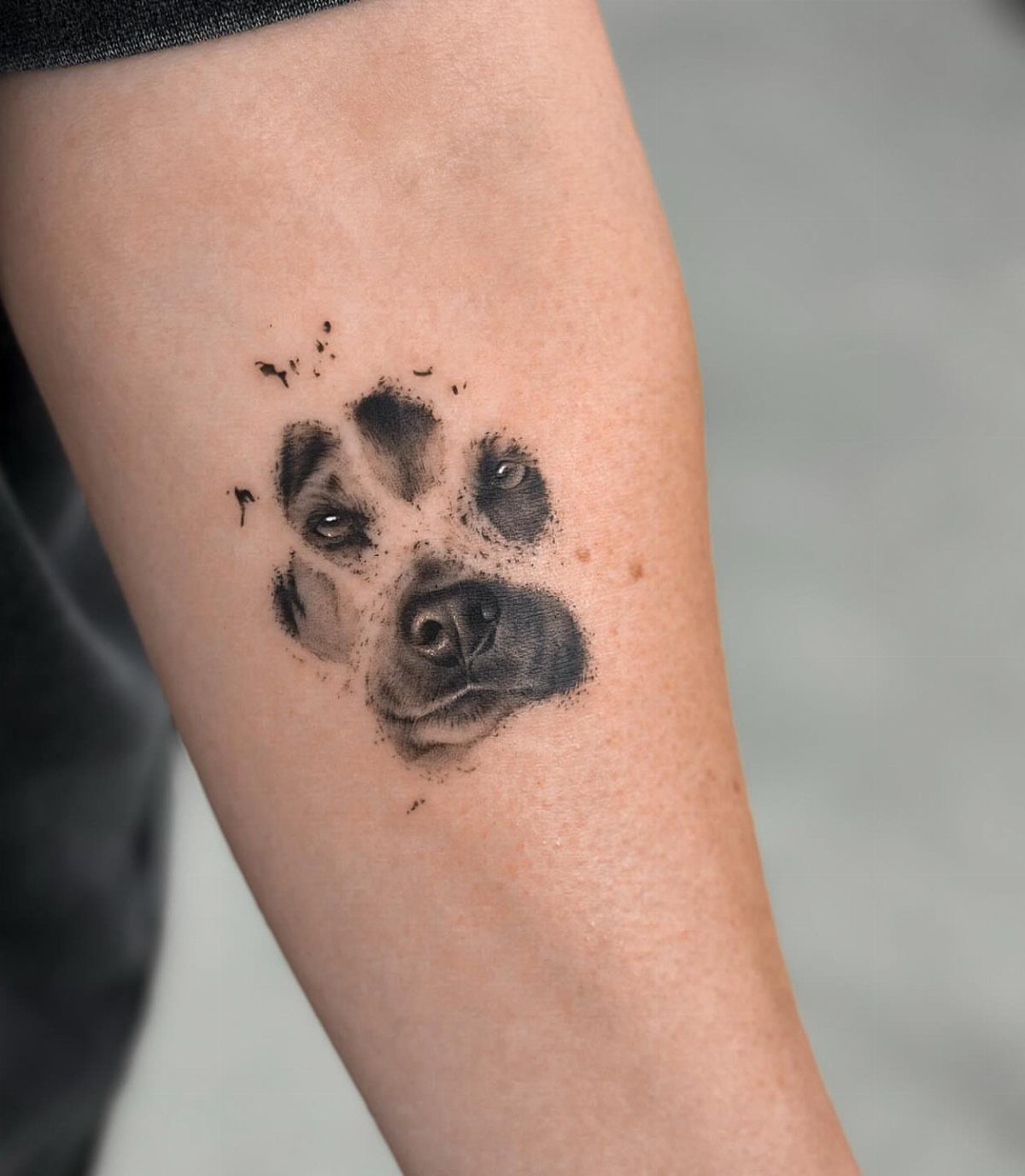 Dog face integrated into a paw print tattoo on a person's forearm