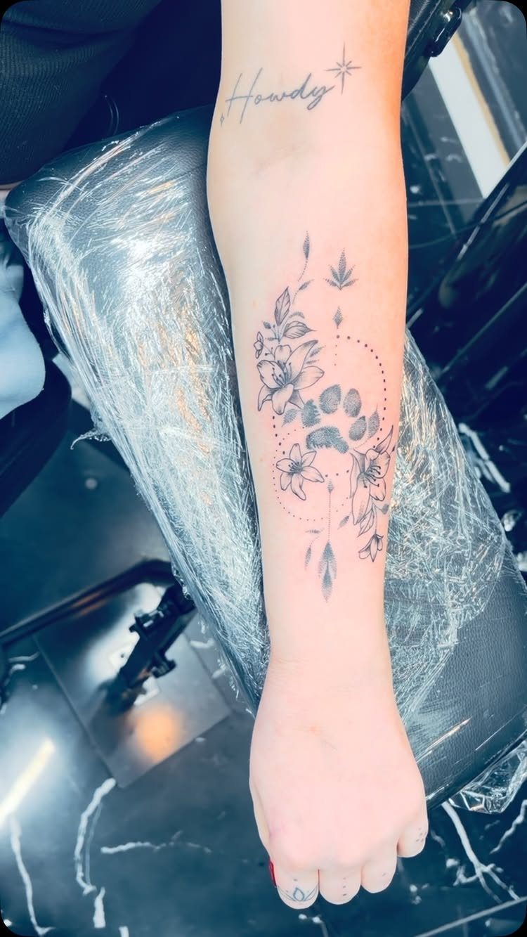 Floral paw print tattoo on a forearm with delicate flowers and leaves.