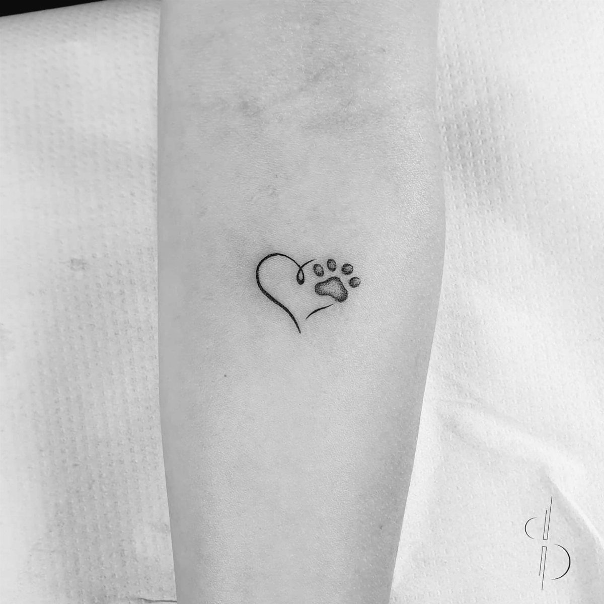Small black ink tattoo of a dog paw print with a heart shaped pad.