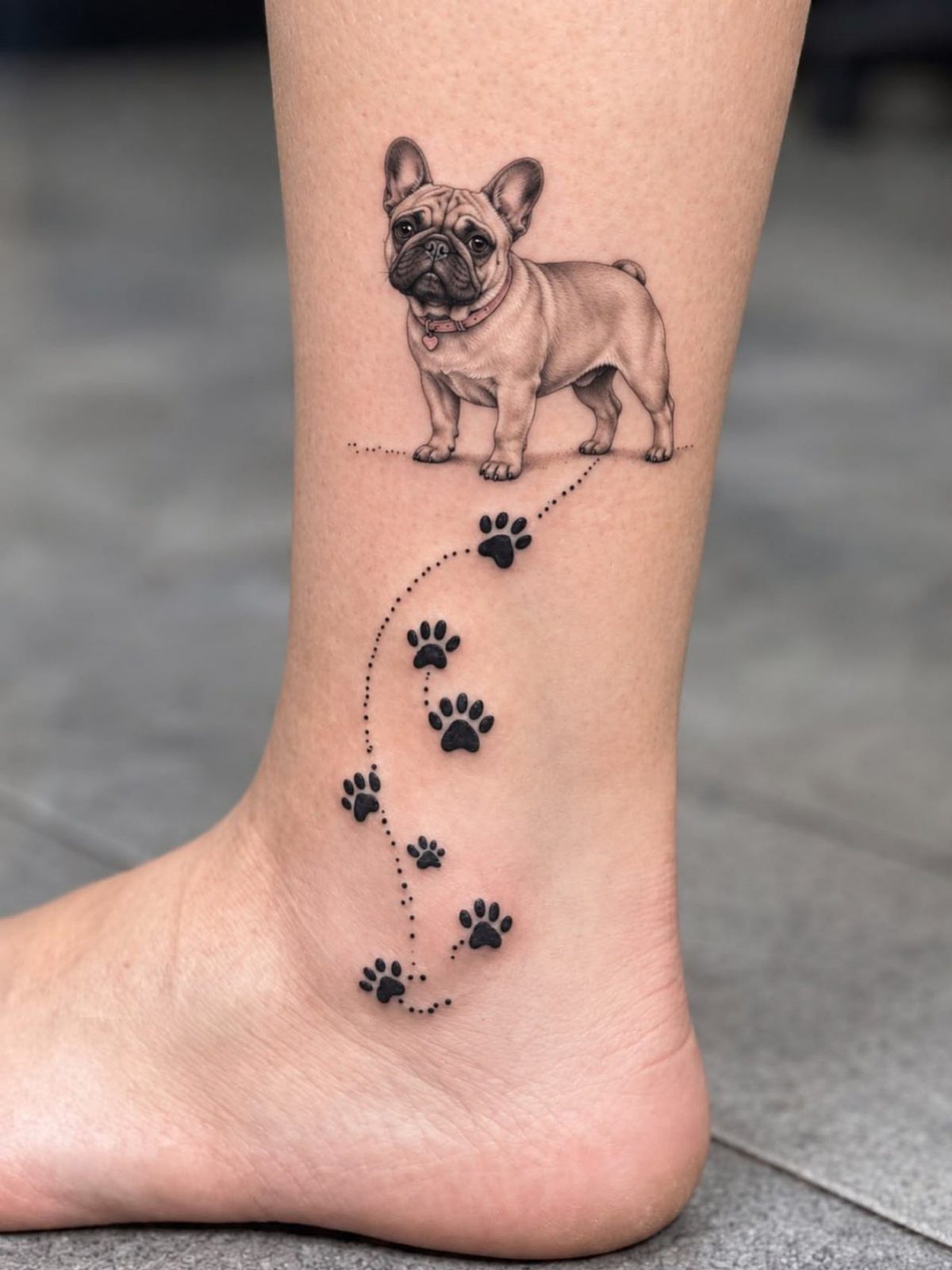 French Bulldog tattoo with a trail of paw prints on a person's ankle