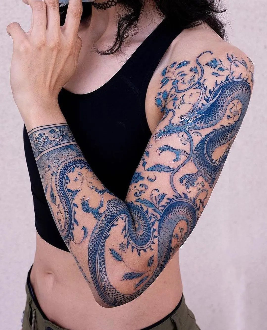 Blue dragon sleeve tattoo winding from shoulder to wrist with floral accents