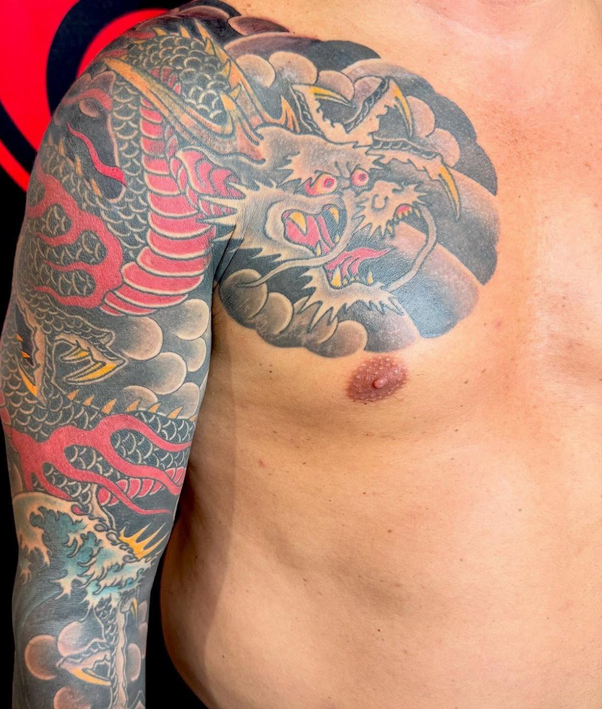 Japanese dragon tattoo winding down an arm with grey clouds and blue waves