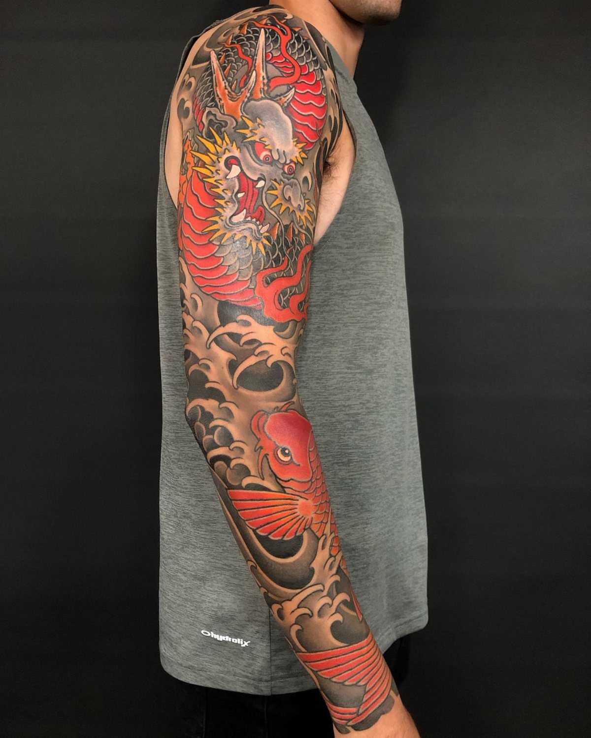 Full sleeve tattoo featuring a red Japanese dragon and koi fish with waves.