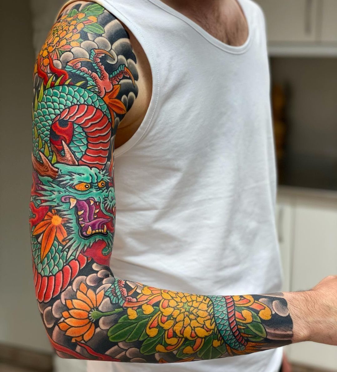 Colorful dragon sleeve tattoo with orange flowers and grey clouds on a man's arm