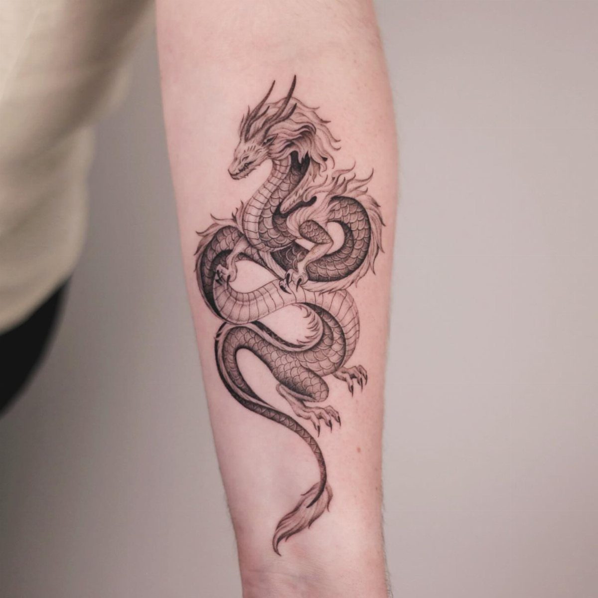 Black ink dragon tattoo on a person's forearm with detailed scales and curves.