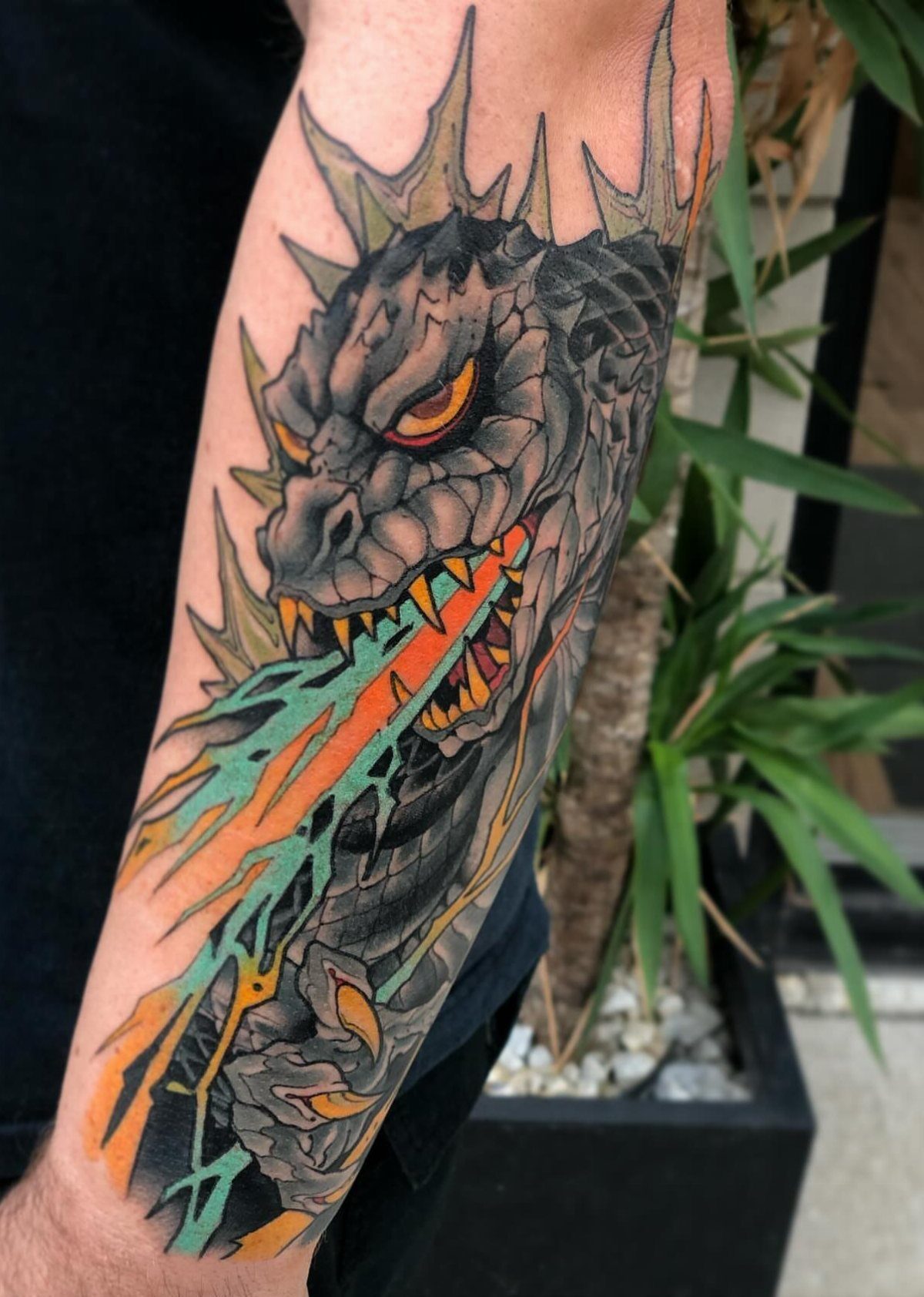 Dragon tattoo on a forearm breathing orange and teal fire with sharp spikes.