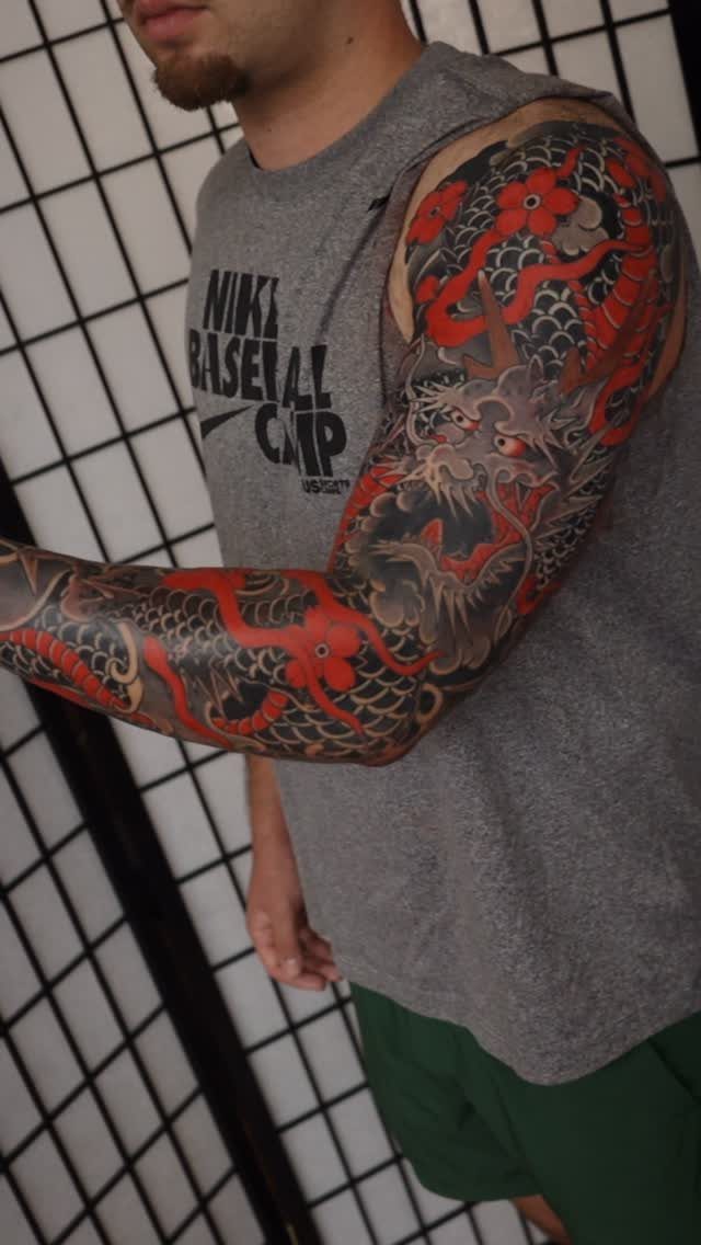 Red and grey dragon tattoo sleeve with red flowers on a man's arm.