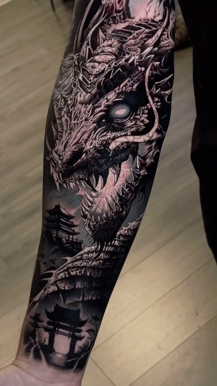 Detailed black and grey dragon tattoo on an arm with Japanese pagodas.