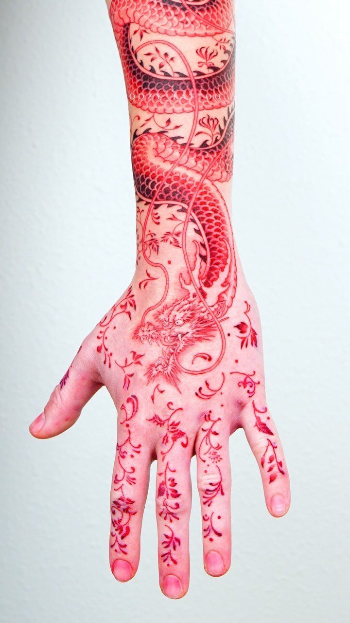 Red ink dragon tattoo winding from a forearm down to the hand.