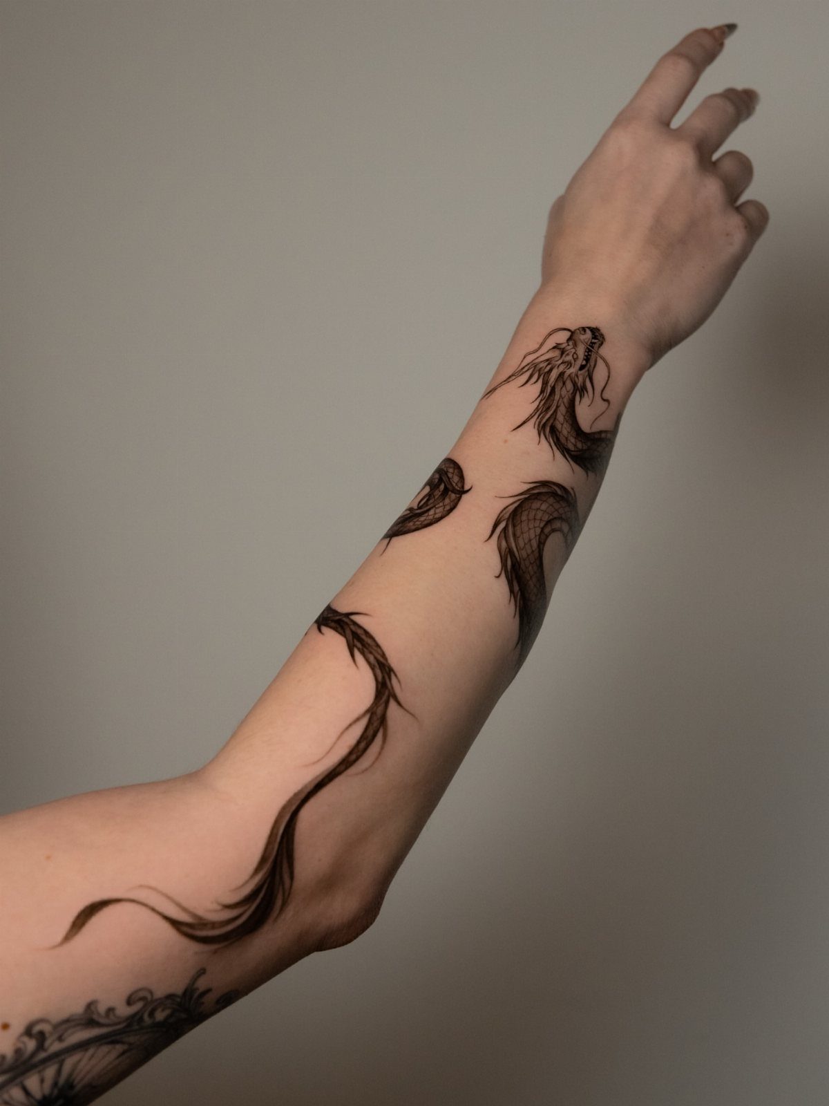 Serpentine dragon tattoo in black ink winding around a person's arm