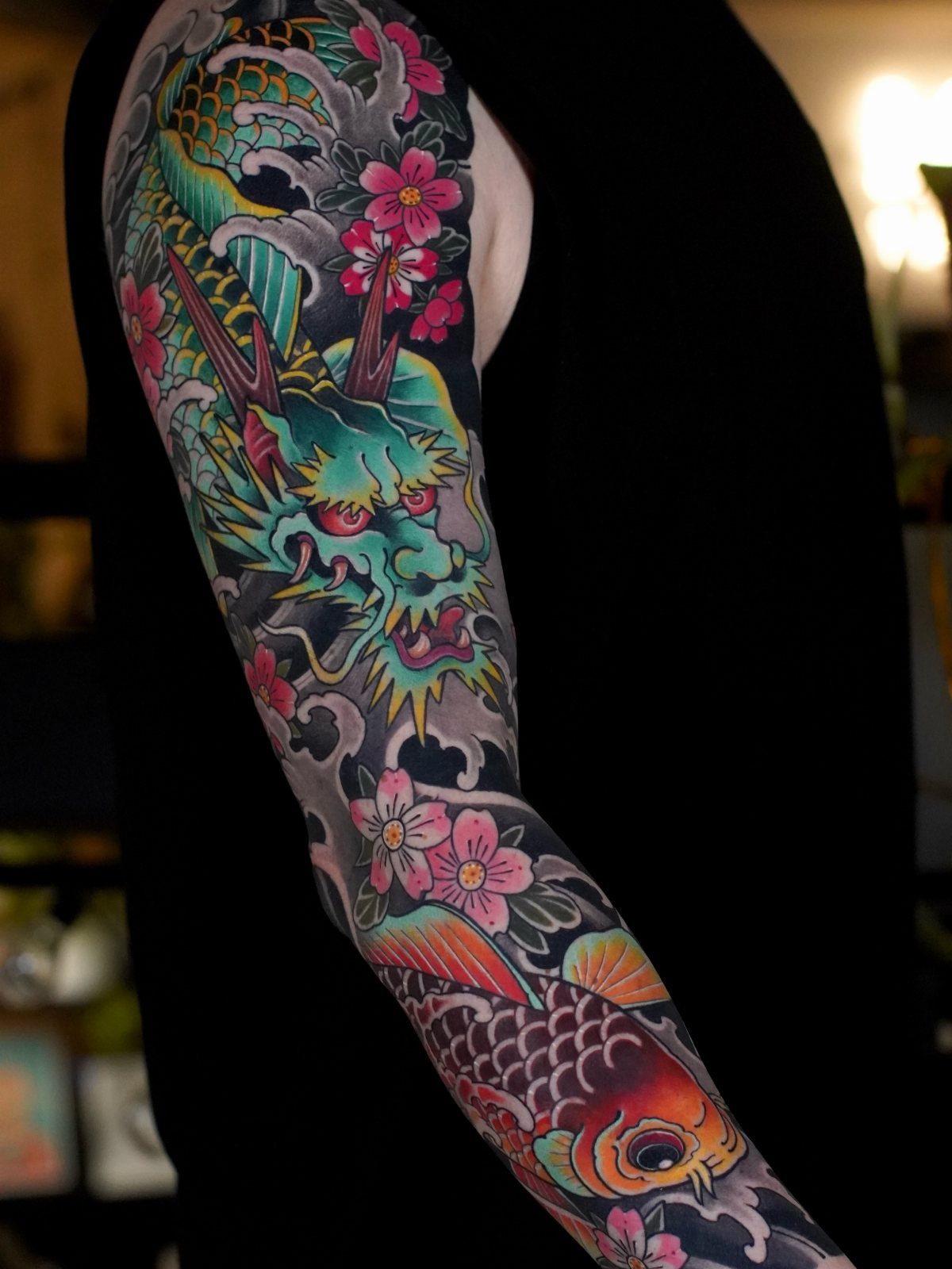 Colorful dragon and koi fish tattoo sleeve with pink flowers and ocean waves.