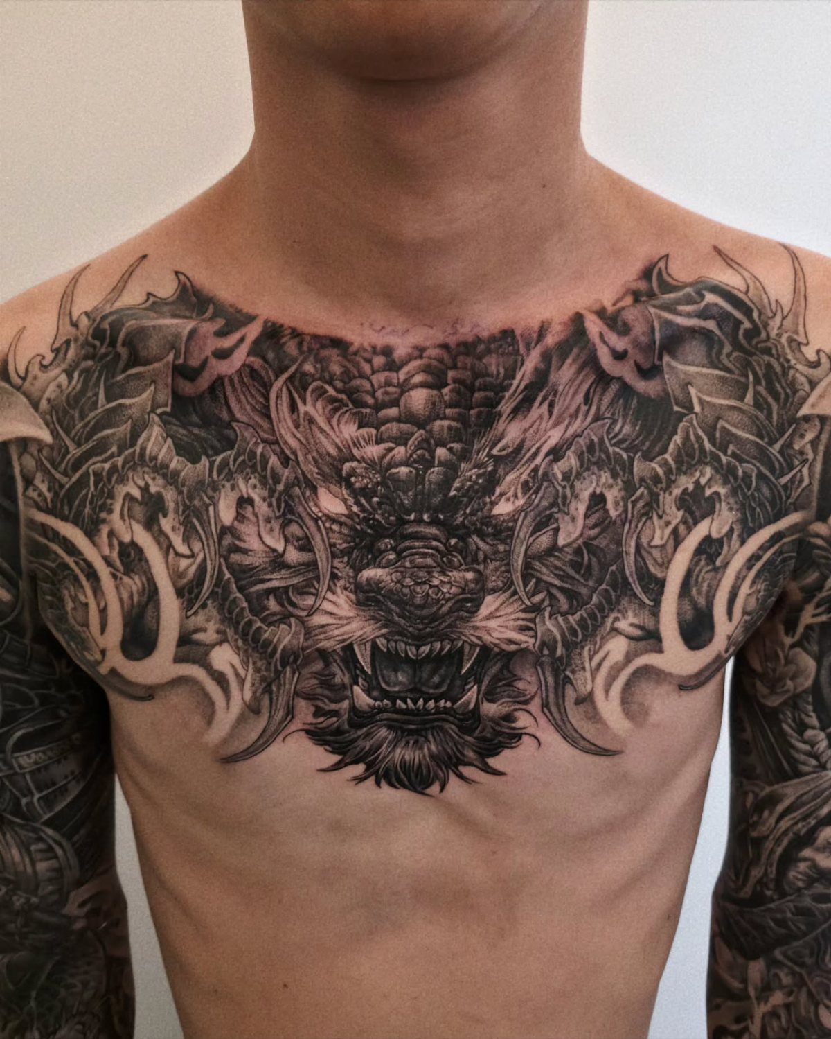 Detailed black and grey dragon tattoo covering a man's chest and collarbones.