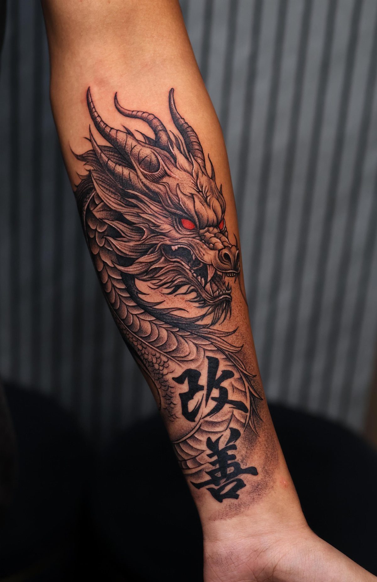 Dragon head tattoo with red eyes and Chinese characters on a forearm.