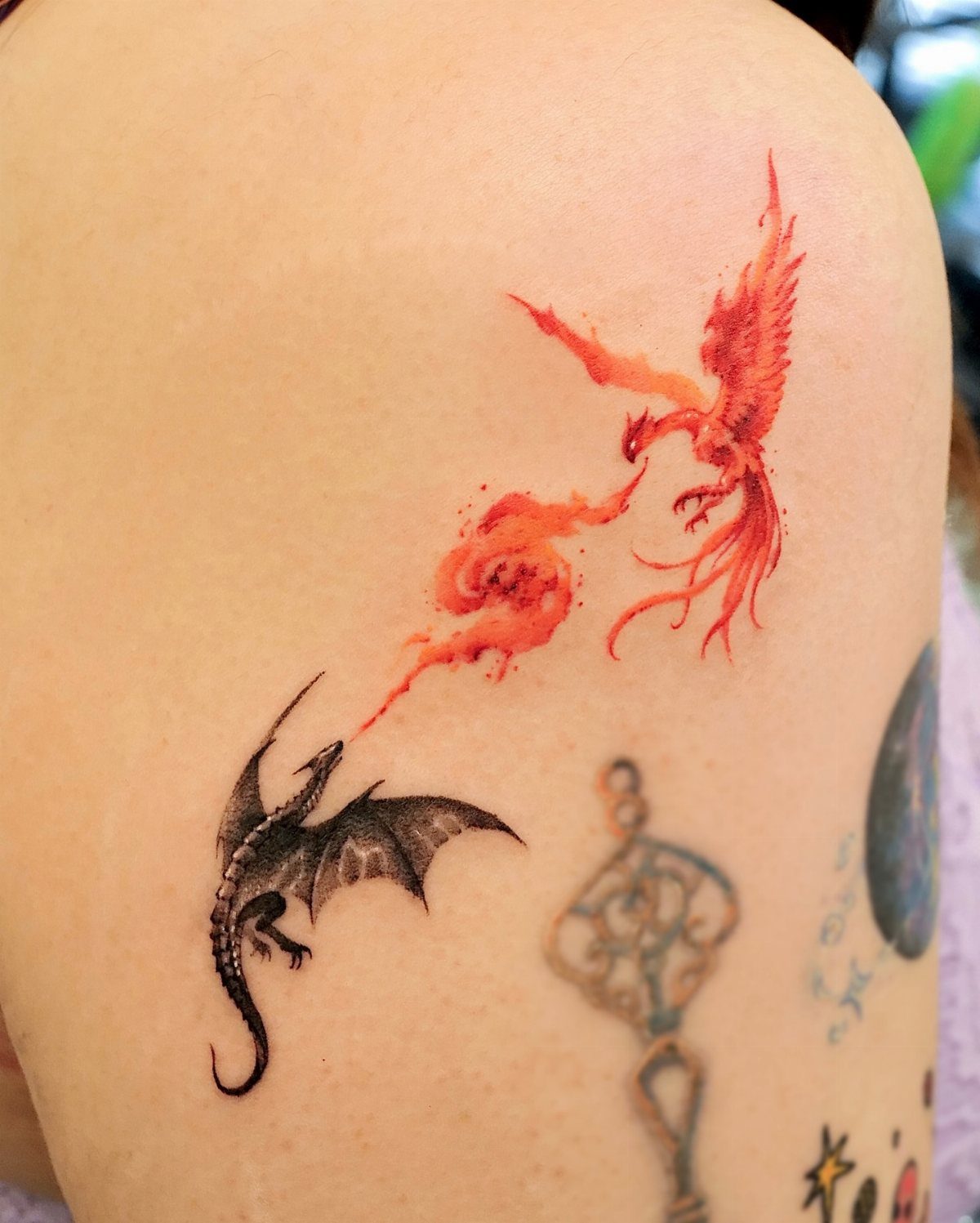 Black dragon and red phoenix tattoo on a person's shoulder with fire effects.