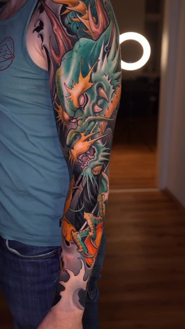 Colorful dragon sleeve tattoo covering a person's arm from shoulder to wrist.