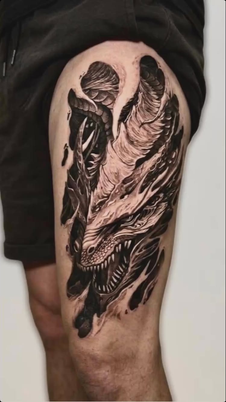 Fierce dragon head tattoo in black and grey ink on a person's thigh
