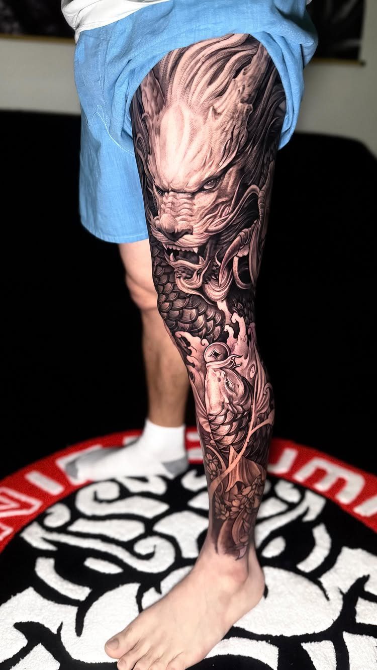 Detailed black and grey dragon tattoo covering the entire leg of a person.