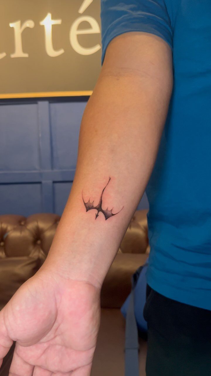 Small black minimalist dragon tattoo on a person's inner forearm
