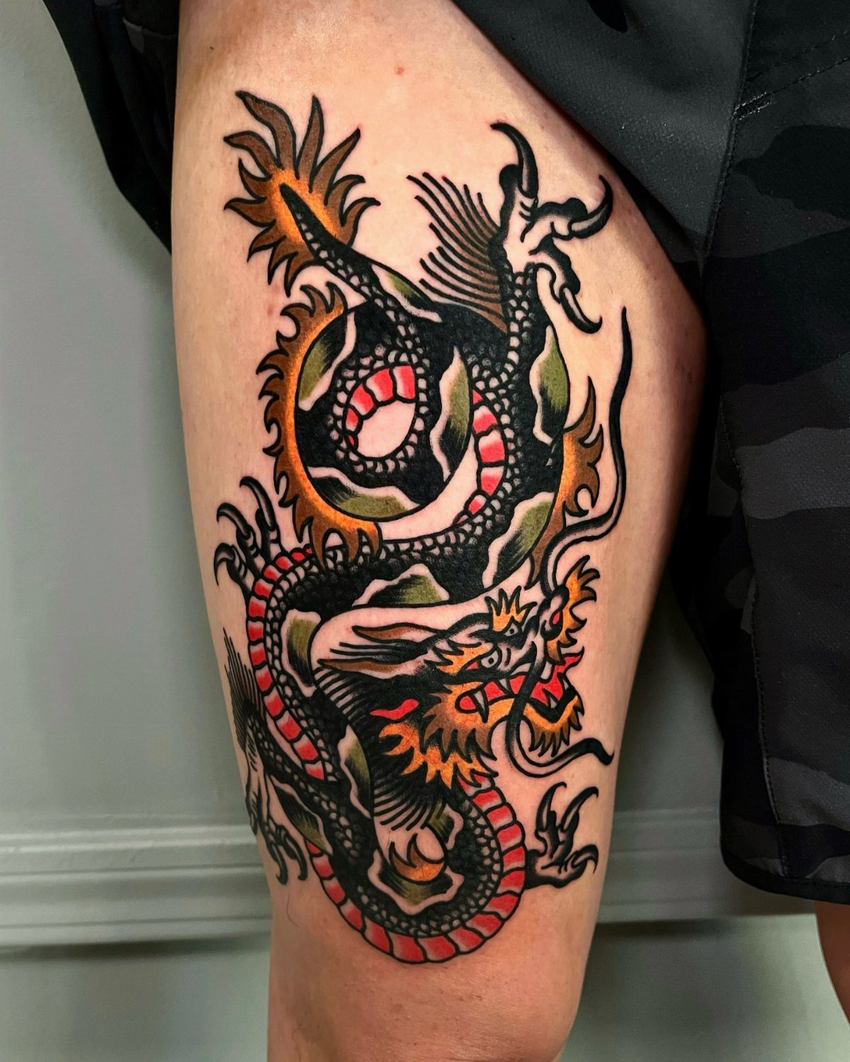 Dragon tattoo on a thigh with bold lines and red and orange colors