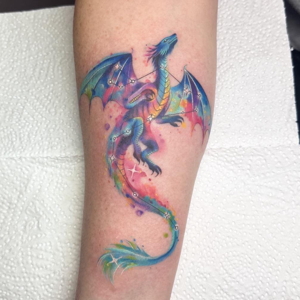 Watercolor dragon tattoo on a forearm with vibrant blue and pink cosmic splashes