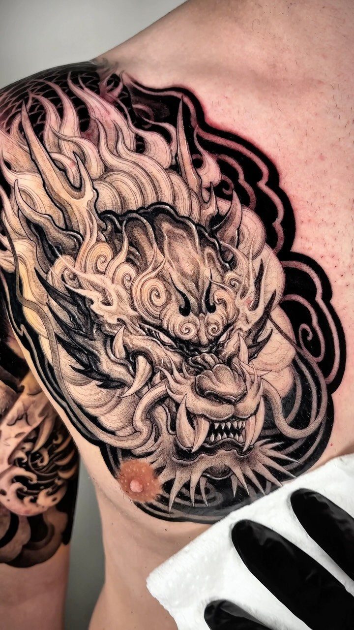 Detailed black and grey dragon head tattoo on a man's chest and shoulder.