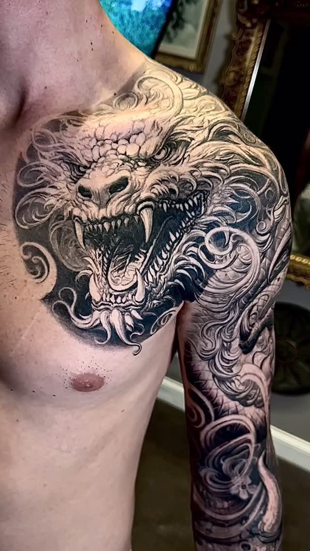 Detailed black and grey dragon tattoo covering a man's chest, shoulder, and arm.