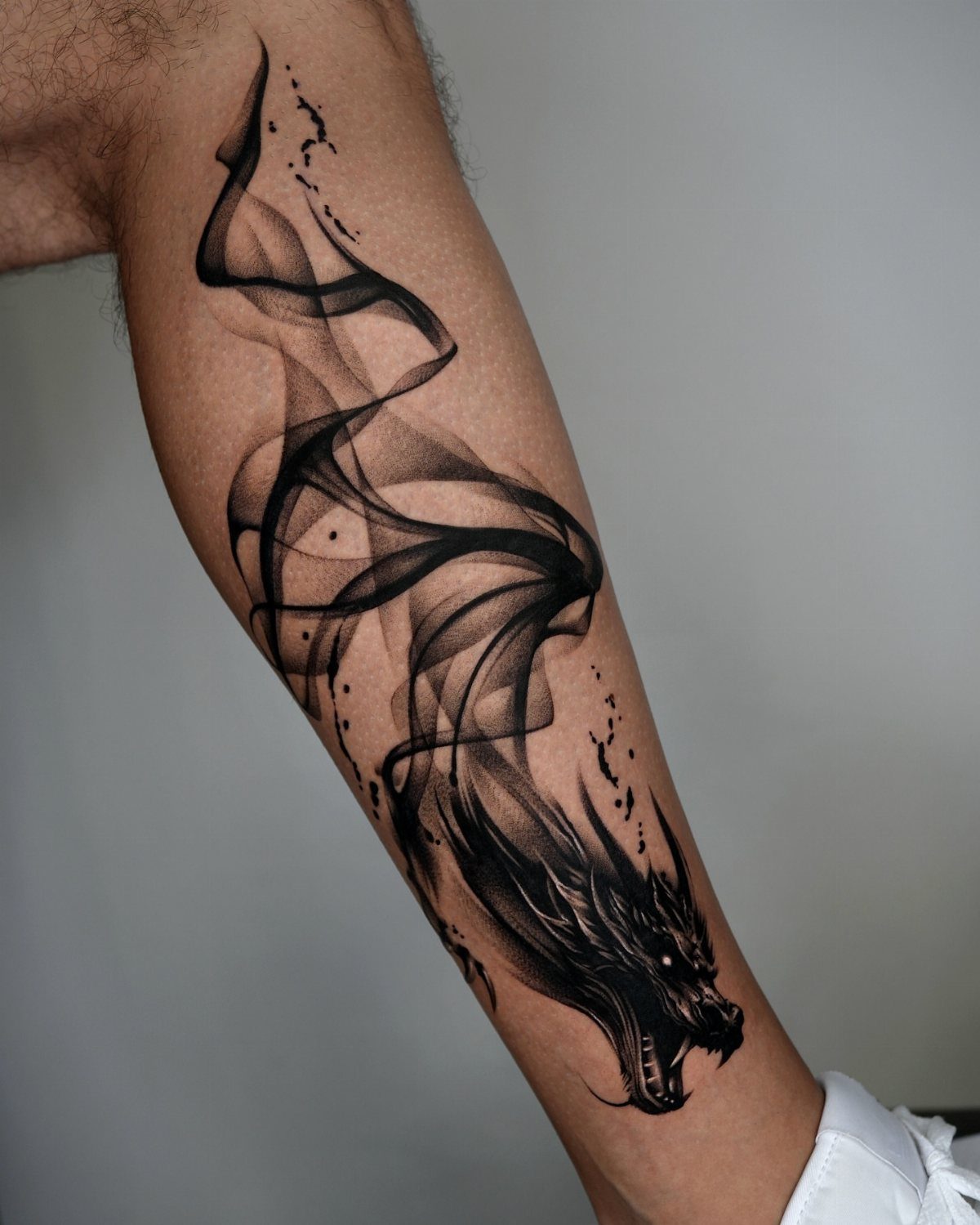 Black ink dragon tattoo with smoke-like patterns on a man's forearm