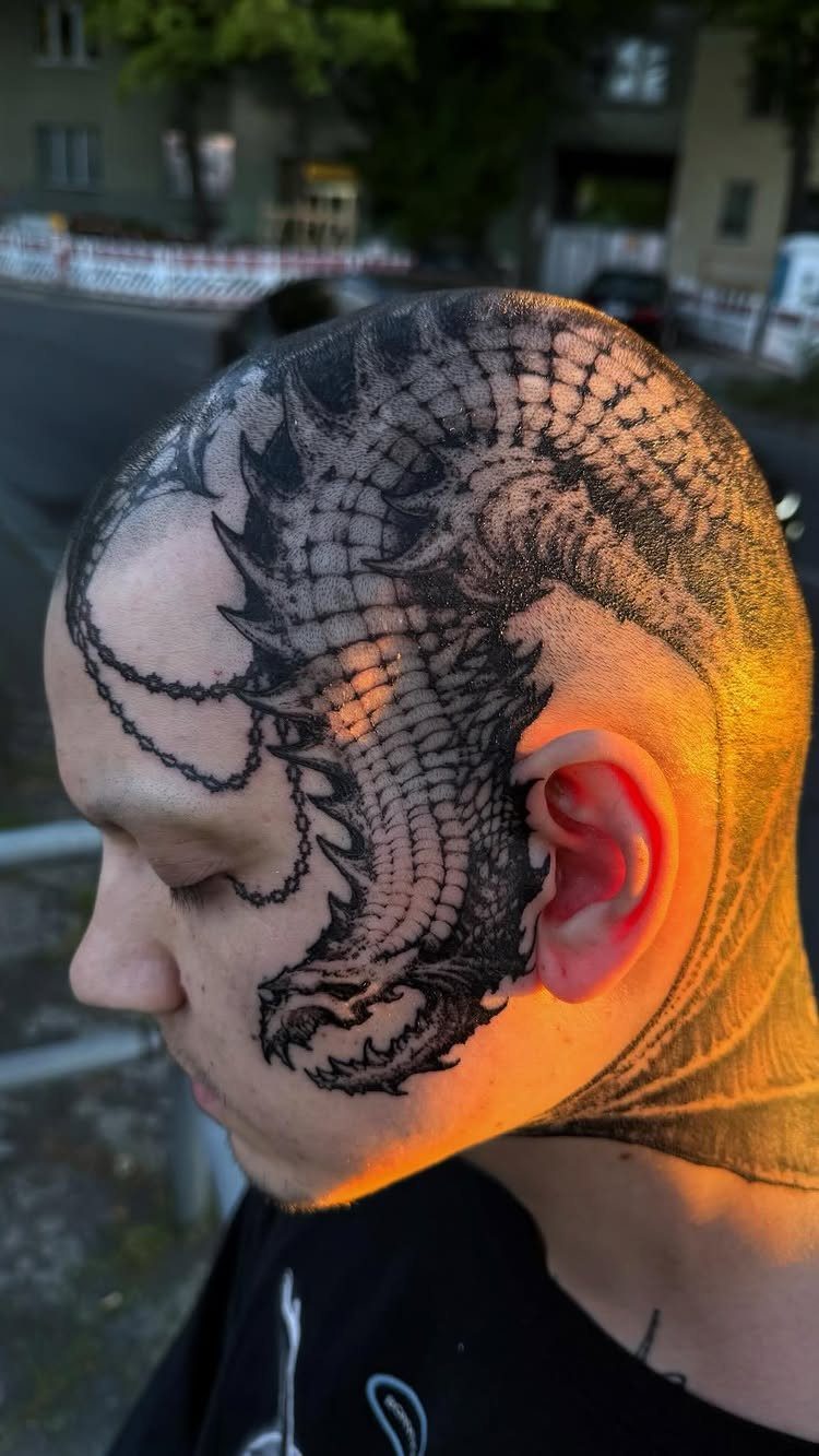 Detailed black ink dragon head tattoo covering a bald man's scalp and temple.