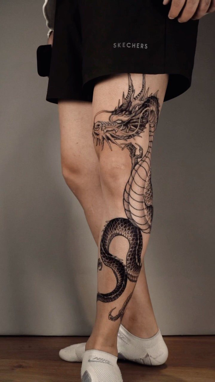 Black ink dragon tattoo winding down a person's lower leg and calf.