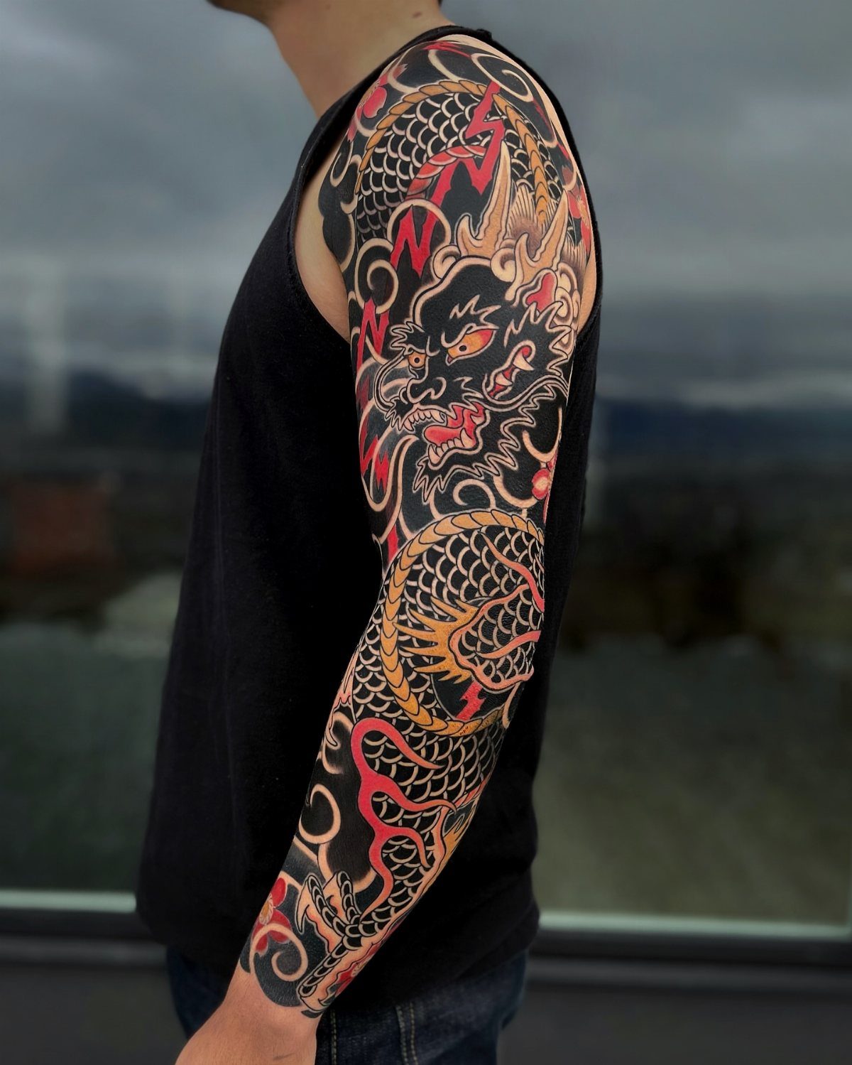 Full sleeve Japanese dragon tattoo in red and black on a man's arm.