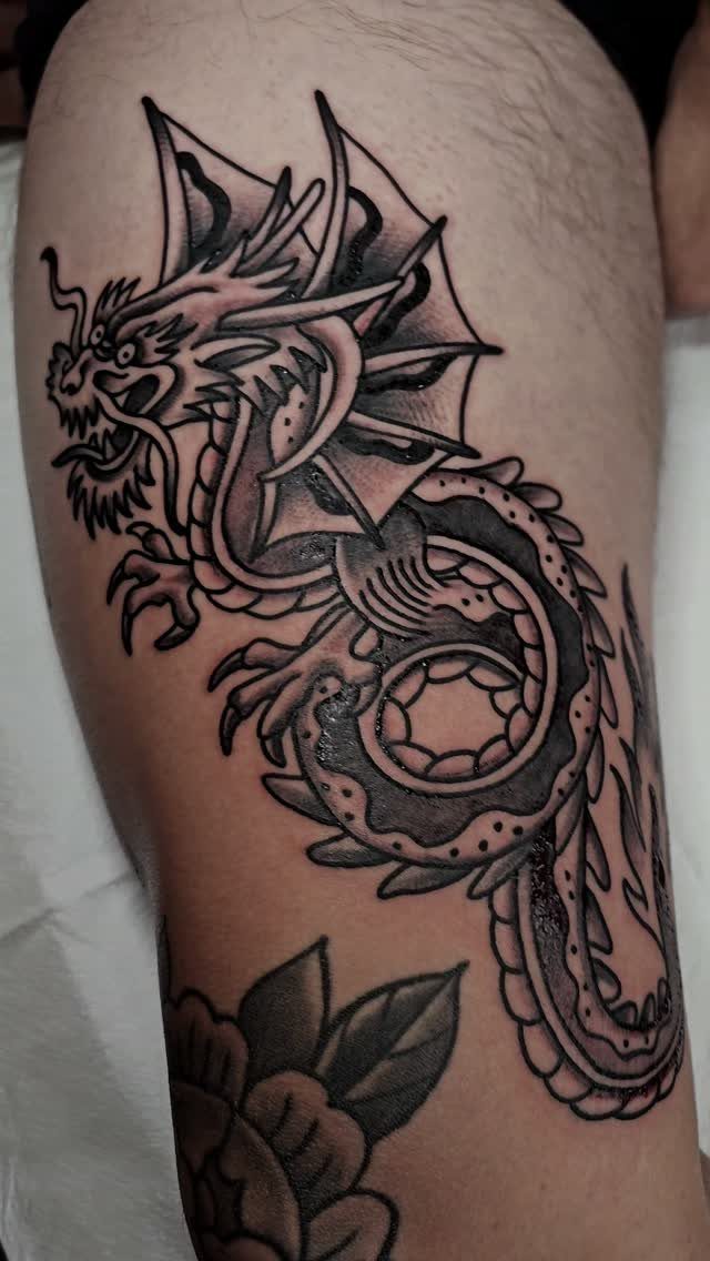 Detailed black and grey dragon tattoo on a man's upper thigh.