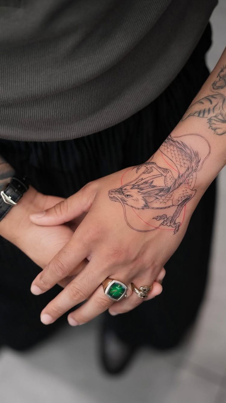 Serpentine dragon tattoo with red accents on a person's hand and wrist.