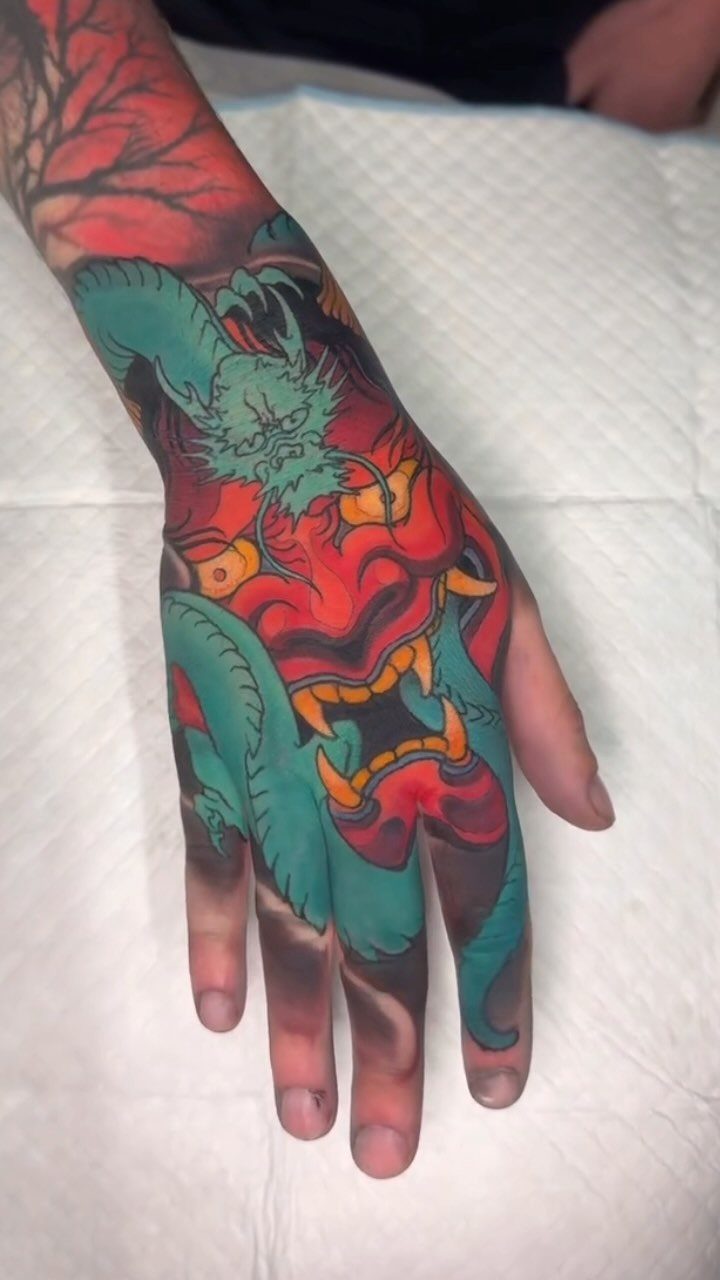 Teal-green dragon and red demon tattoo covering a person's hand and wrist.