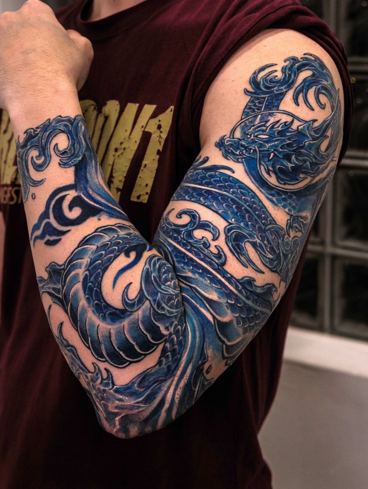 Blue Japanese dragon tattoo covering a man's arm from shoulder to forearm.