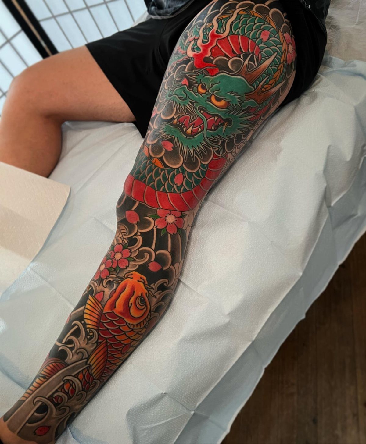 Full leg tattoo featuring a green dragon and a red koi fish.