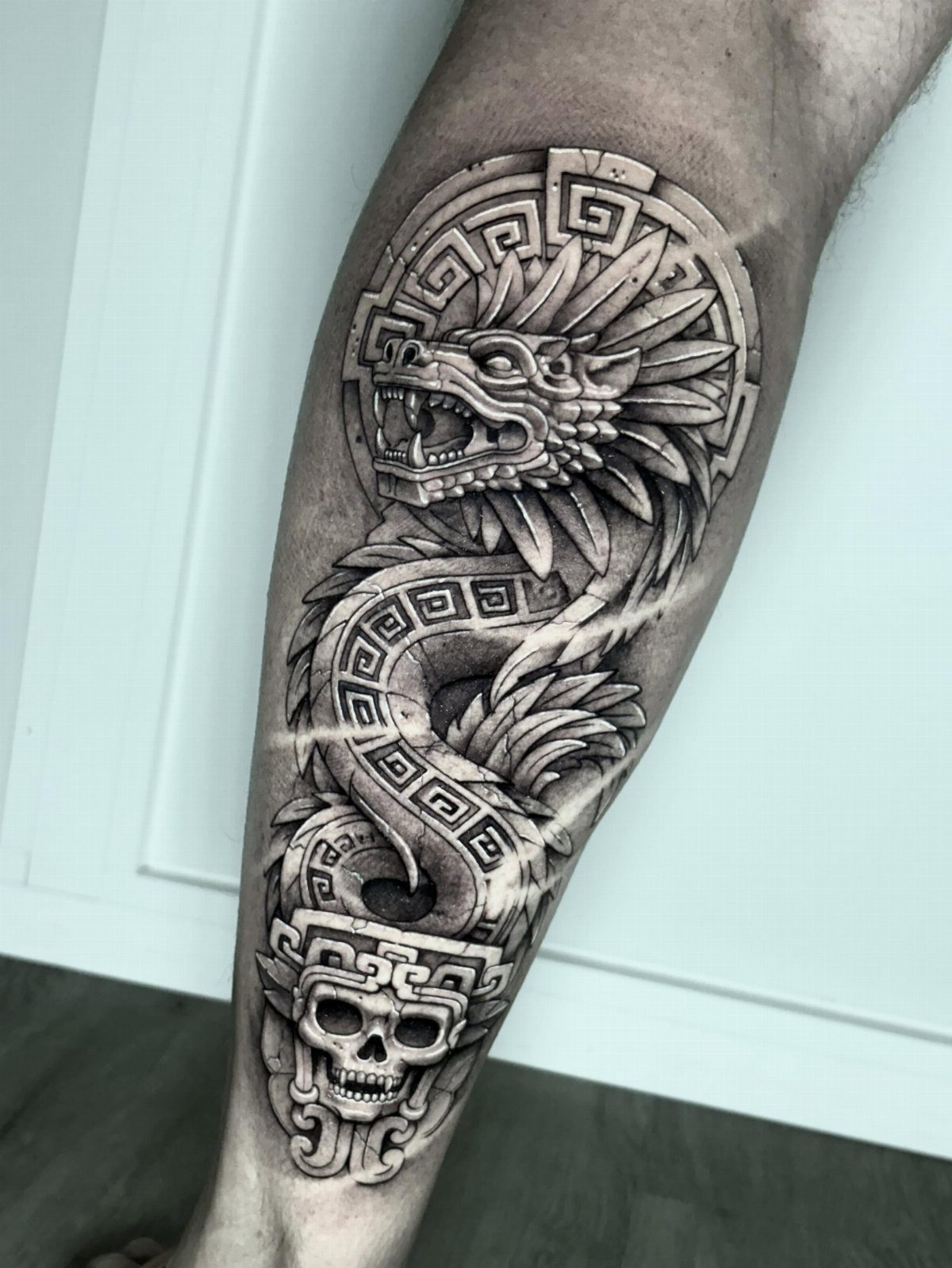 Feathered serpent Quetzalcoatl tattoo with Aztec patterns and a skull on a leg.