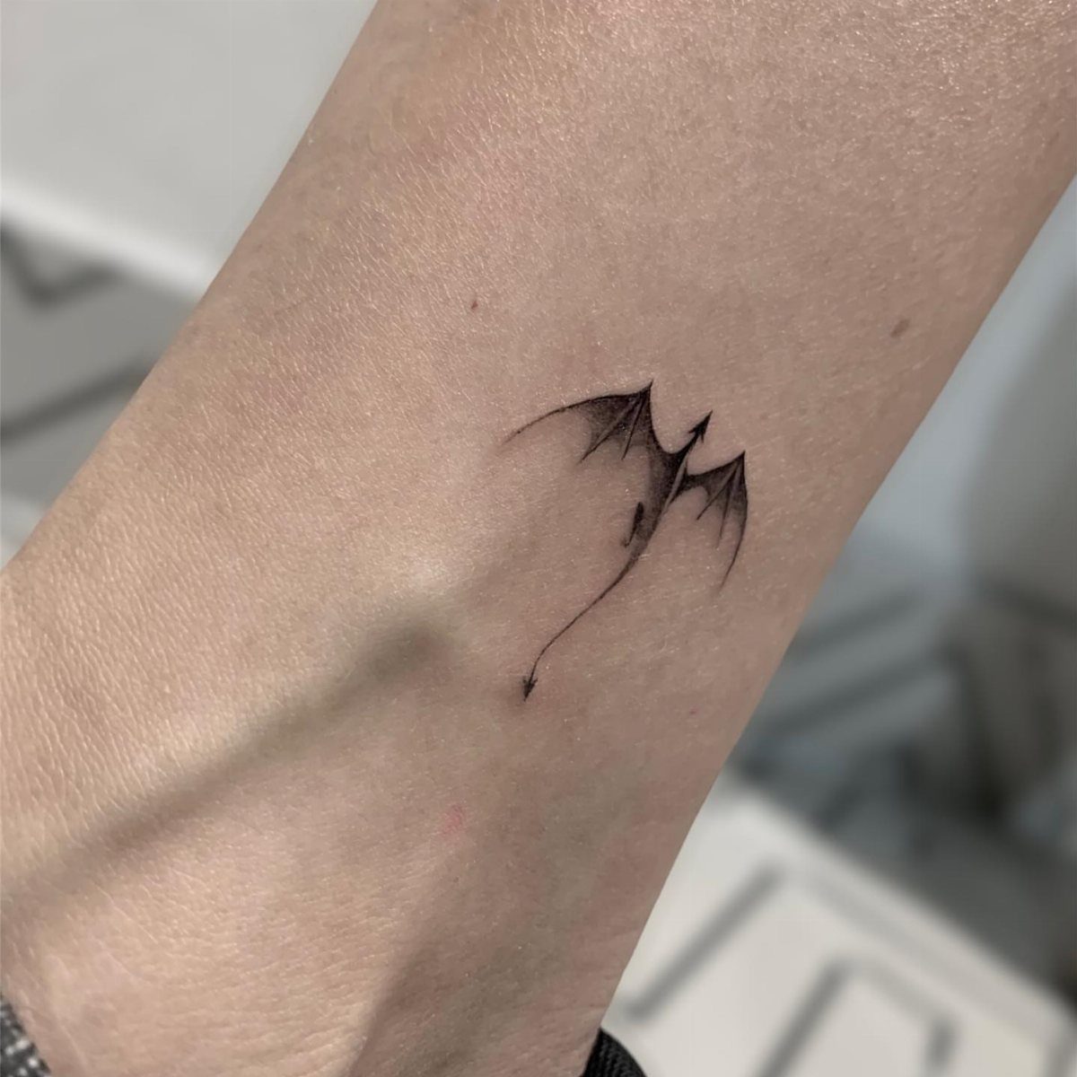 Small black ink dragon silhouette tattoo on a person's forearm.