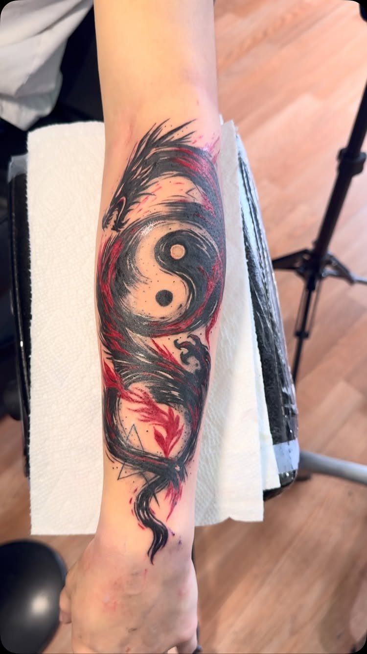 Yin and yang symbol surrounded by two red and black dragons on a forearm