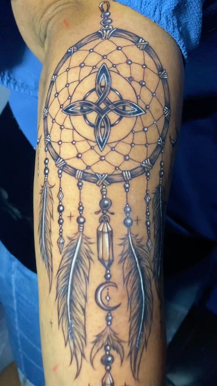 Dreamcatcher tattoo on a forearm featuring a central Celtic knot and hanging feathers.