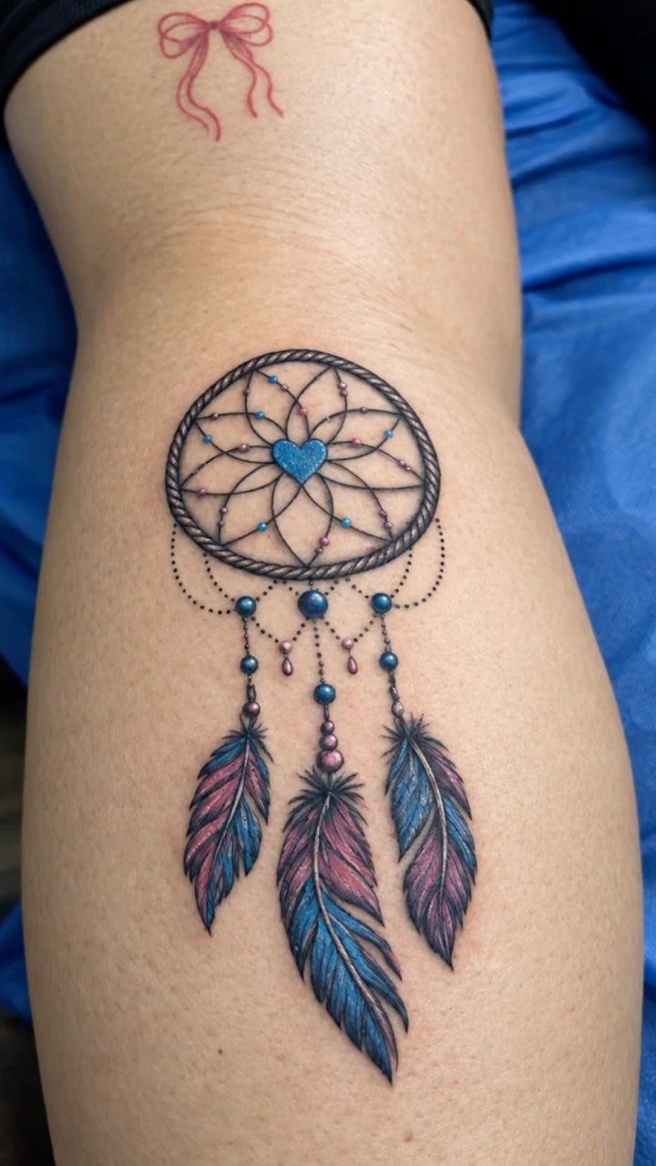 Dreamcatcher tattoo on a leg with a blue heart and colorful feathers