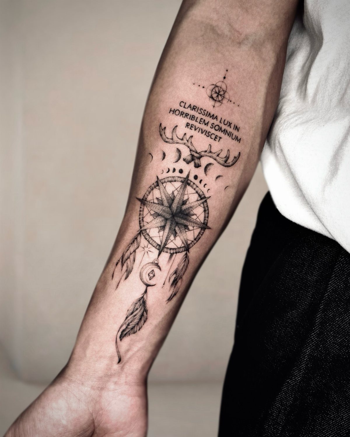 Compass rose dreamcatcher tattoo with feathers and Latin text on a forearm