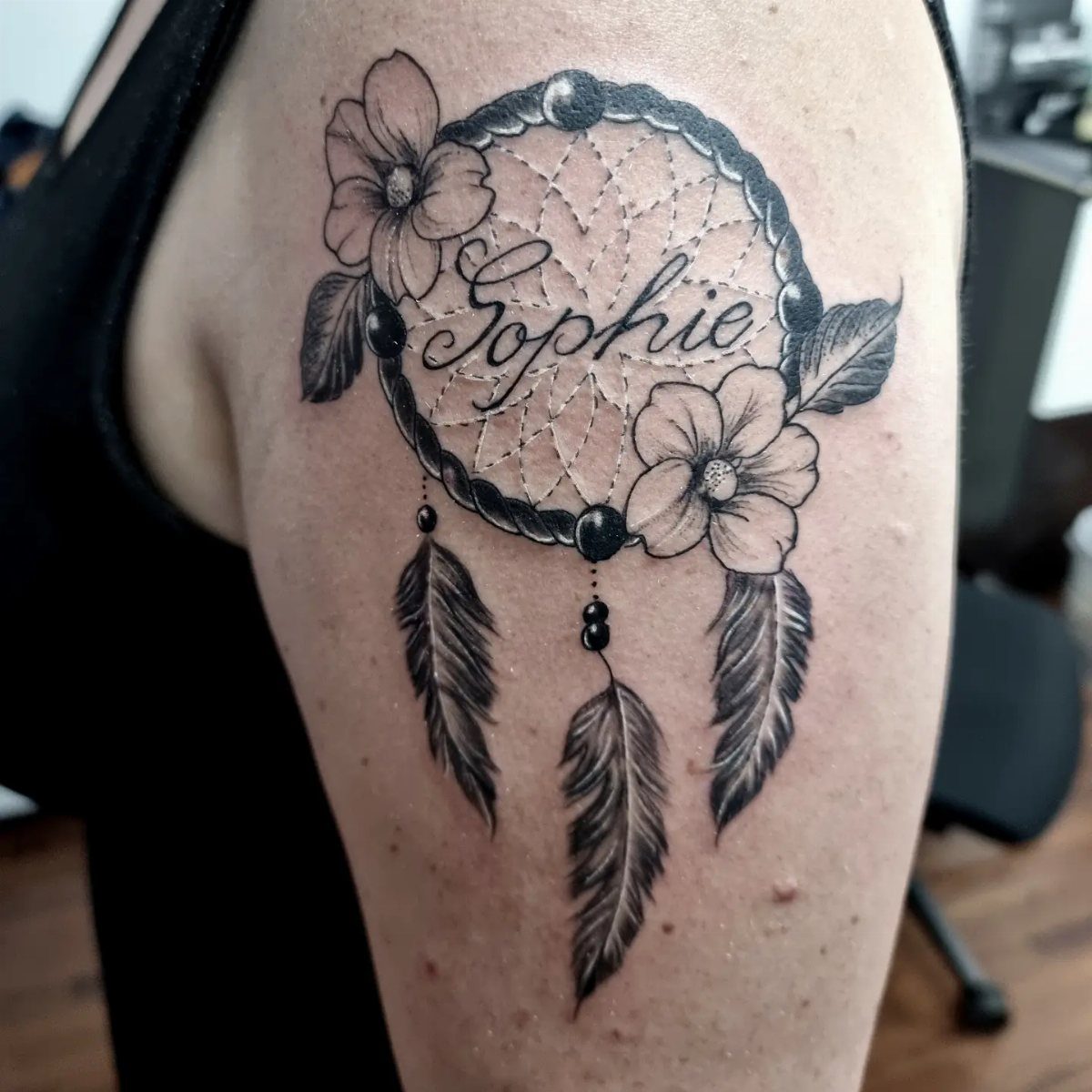 Dreamcatcher tattoo on an arm with the name Sophie and floral accents