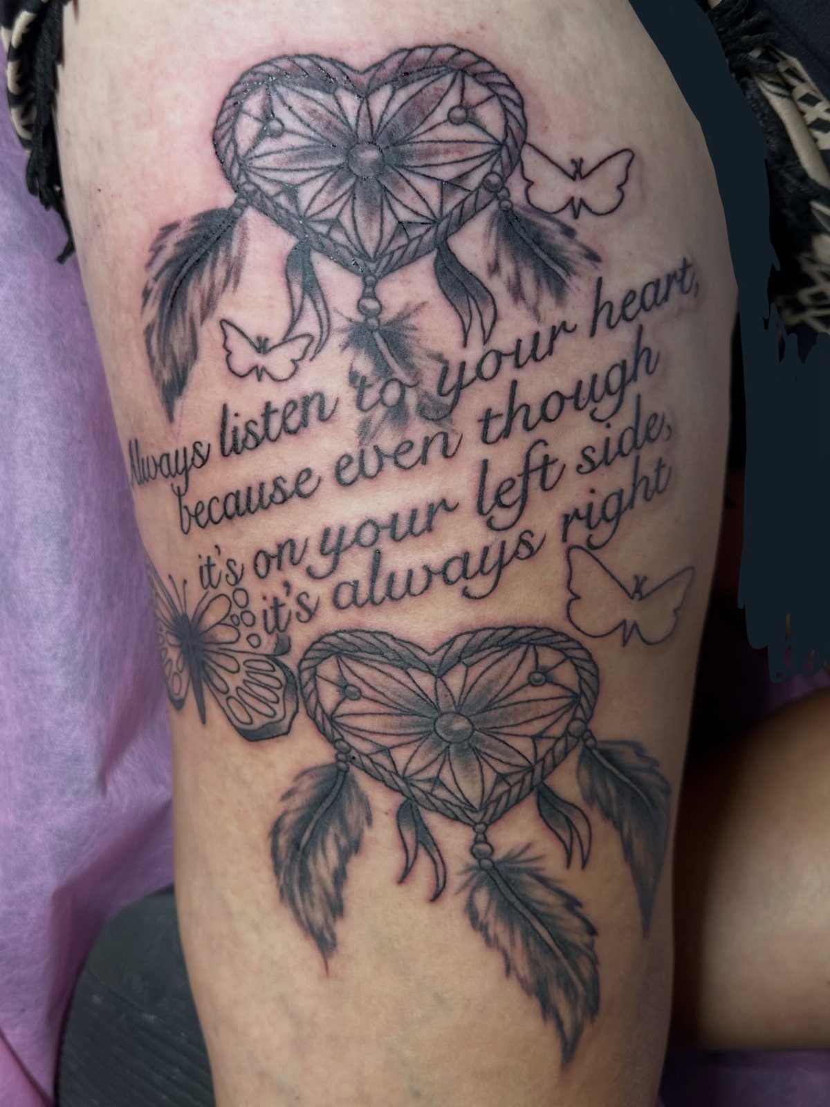 Heart-shaped dreamcatcher tattoos with feathers and butterflies on a person's leg with text.
