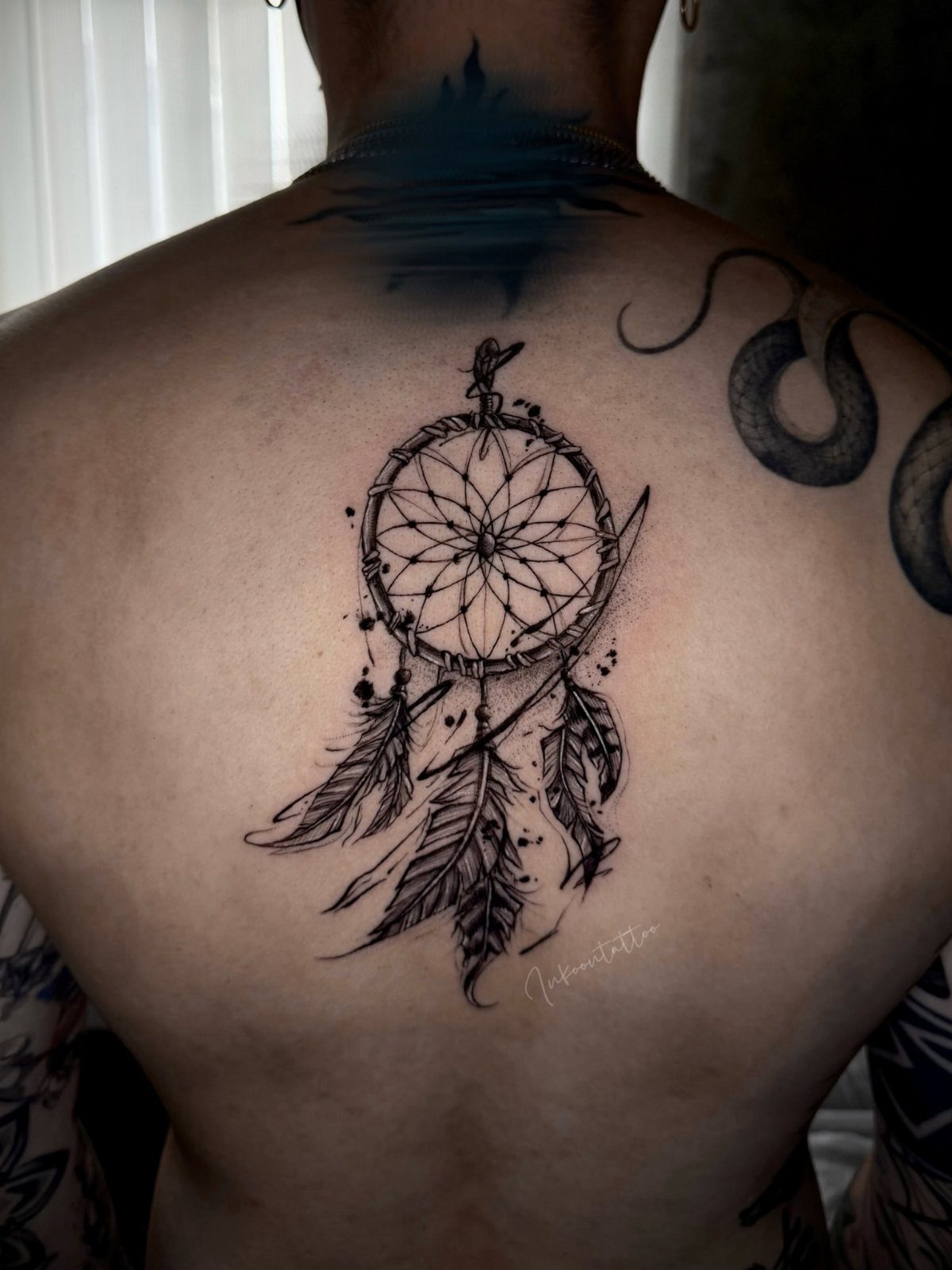 Large dreamcatcher tattoo with detailed feathers on a person's upper back.