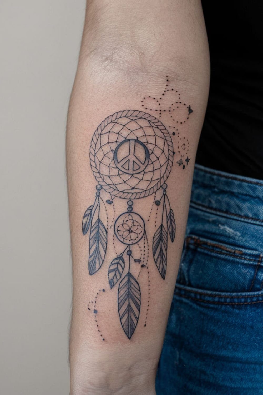 Dreamcatcher tattoo on a forearm featuring a peace sign and hanging feathers.