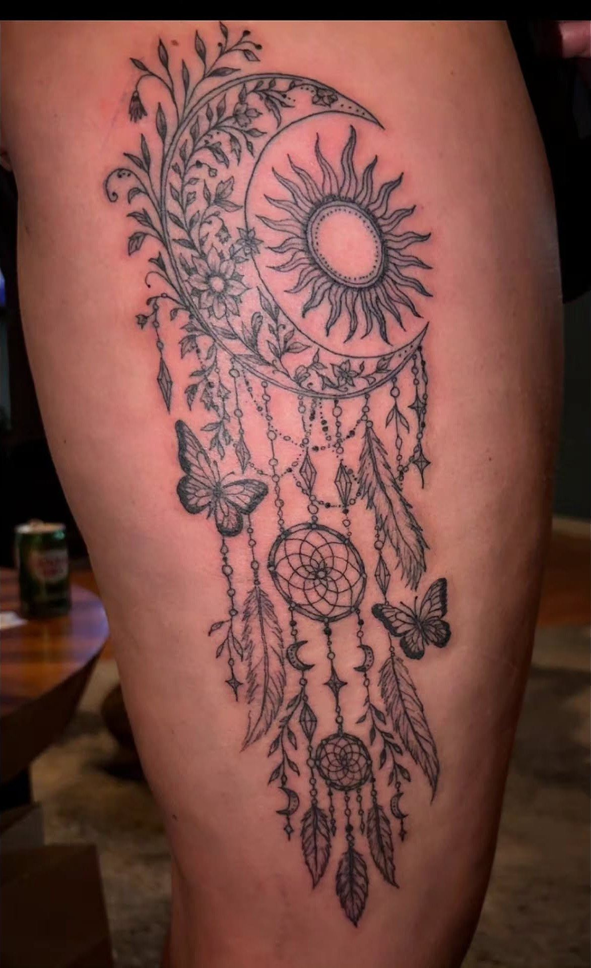 Dreamcatcher tattoo on a thigh featuring a sun, crescent moon, and butterflies.