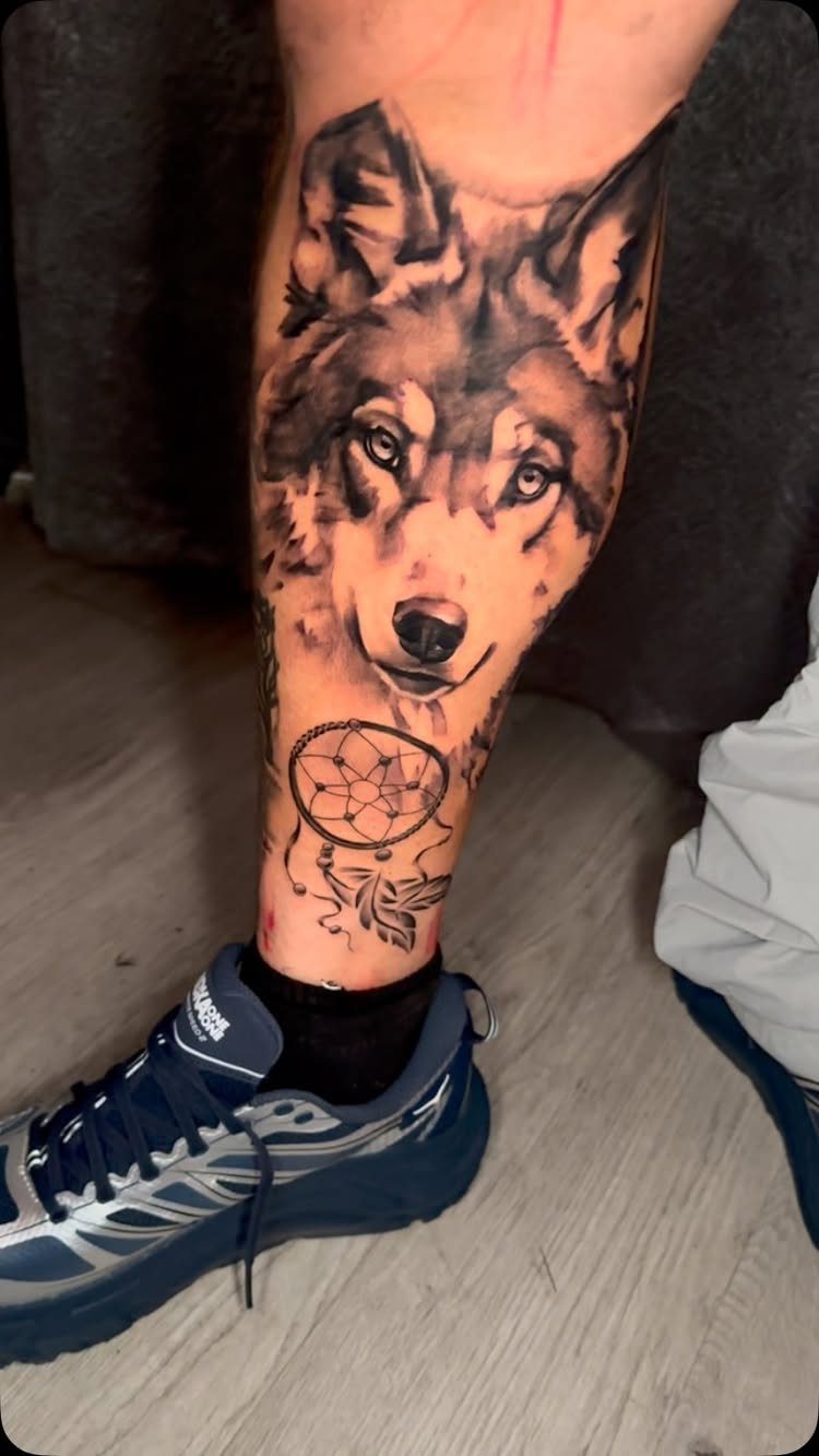 Wolf and dreamcatcher tattoo on a lower leg above a blue sneaker