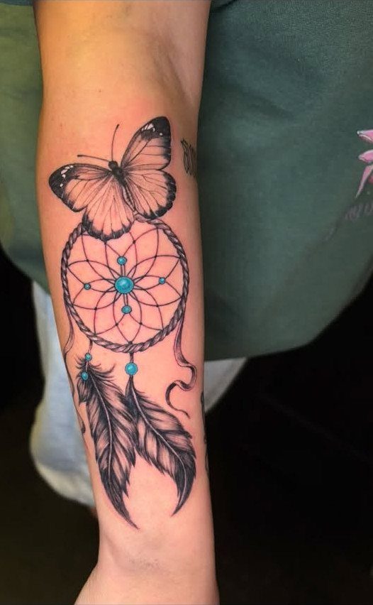 Dreamcatcher tattoo with a butterfly and feathers on a person's forearm