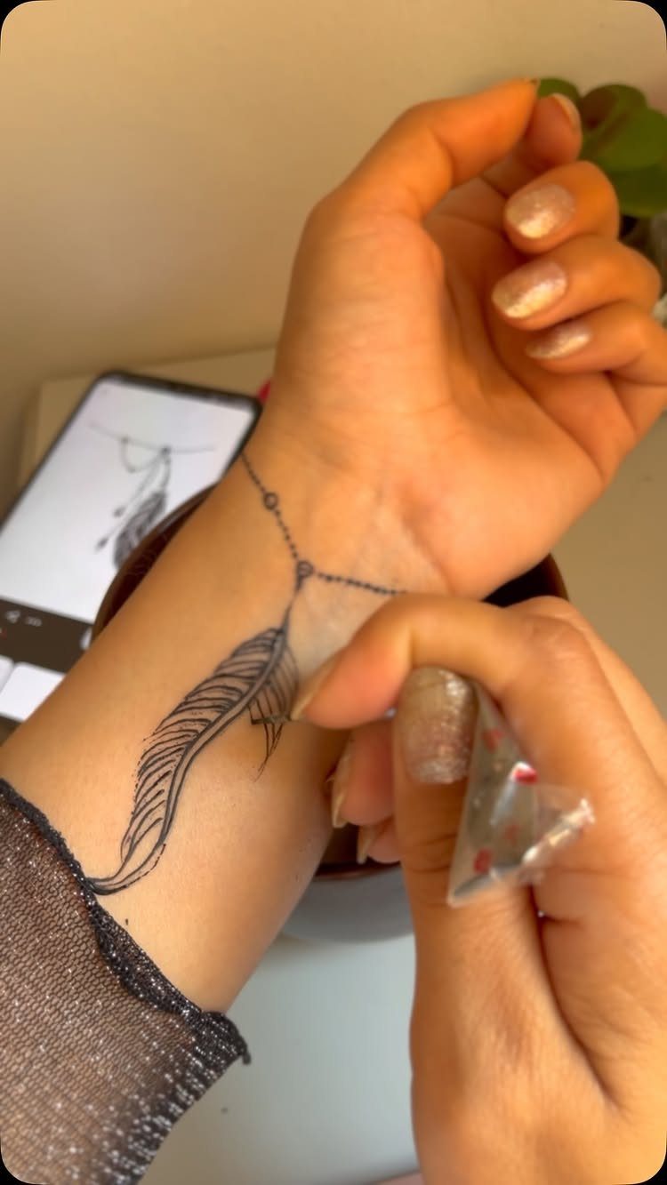 Feather tattoo design on a wrist with a delicate chain detail
