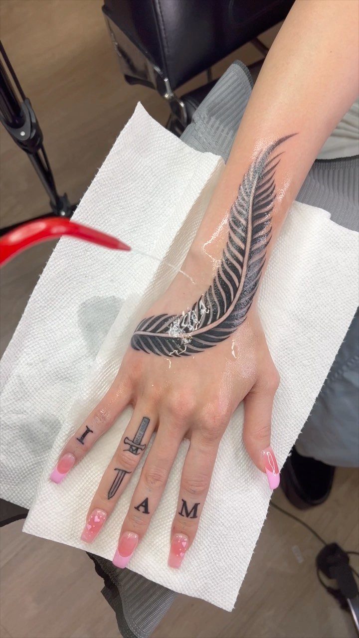 Feather tattoo on a person's wrist and hand resting on a white towel